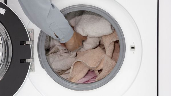 Mano che inserisce asciugamani colorati nel cestello di una lavatrice a carica frontale.