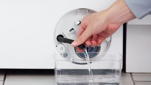 Mano che raccoglie l’acqua dal tubo di scarico della lavatrice all’interno di un contenitore trasparente.