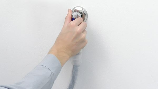 Mano che regola il rubinetto dell’acqua a cui è collegato il tubo di una lavatrice.