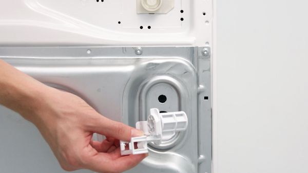 Mano che rimuove il blocco di sicurezza per il trasporto dal retro di una lavatrice.