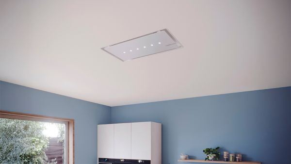 Монтиран на тавана кухненски аспиратор, интегриран в модерна кухня със сини стени и бели шкафове.