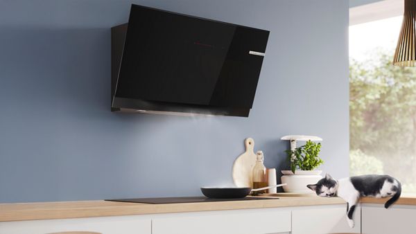 Модерна кухня с черен стенен аспиратор и котка, лежаща спокойно върху кухненски плот.