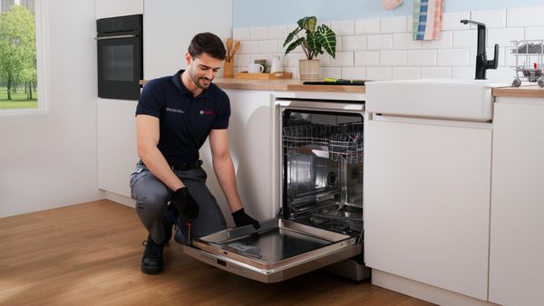 Cocina moderna con electrodomésticos, armarios y un técnico que repara un lavavajillas.