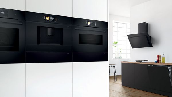 Cuisine élégante noire et blanche, avec de nombreux appareils électroménagers : four, machine à café, hottes aspirante, la-vaisselle, plaque de cuisson