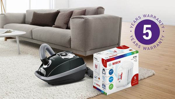 St&oslash;vsuger og dens poser i en lys stue ved siden af en sofa, 5 &aring;rs garanti-logo &oslash;verst p&aring; billedet.