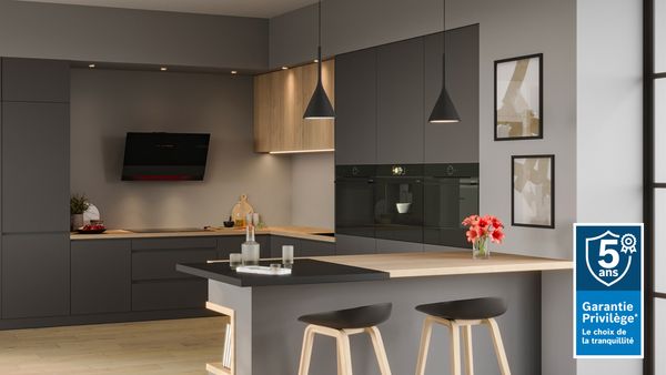 Cuisine moderne ouverte, avec appareils électroménagers noirs et meubles gris et bois clair 