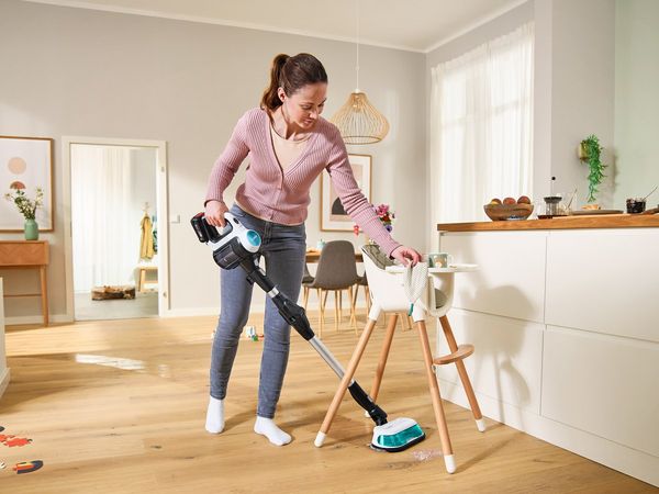 A woman vacuuming the kitchen floor, surrounded by cabinets and appliances. 