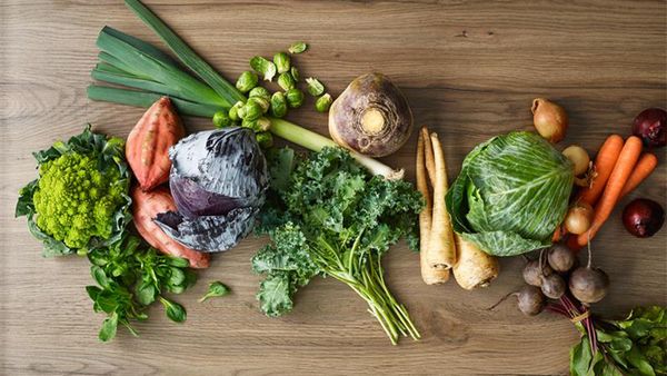 Auf einer Holzoberfläche liegt verschiedenes Wintergemüse, darunter Romanesco, Süßkartoffeln, Rotkohl, Porree, Rosenkohl, Grünkohl, Sellerie, Pastinaken, Weißkohl, Zwiebeln, Schwarzwurzeln und Mohrrüben.