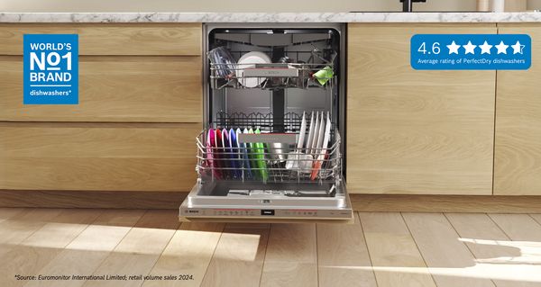 Open Bosch-vaatwasser met kleurrijke borden erin, geplaatst in een moderne keuken met houten kasten.   