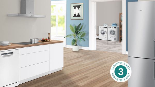 Cuisine ouverte équipée où l'on voit une réfrigérateur, une hotte, un lave-vaisselle, une plaque de cuisson et une buanderie en arrière-plan