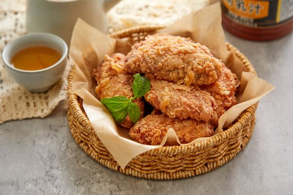 Cestino con pollo fritto servito su carta da forno, accompagnato da una ciotolina di salsa