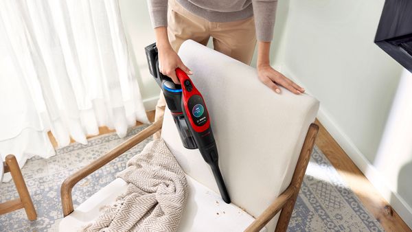 Eine Person saugt mit dem Handteil eines Akku-Staubsaugers Krümel von einem weißen Sessel.