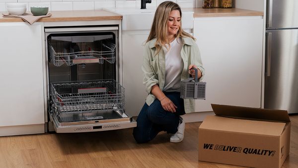 Bosch customer standing next to a dishwasher with a cutlery basket accessory and a delivery box