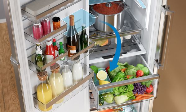 Добре организиран интериор на хладилник показва регулируеми рафтове и отделения на вратата, пълни с напитки, подправки, плодове и зеленчуци, със синя стрелка, подчертаваща гъвкавото разпределение за съхранение.