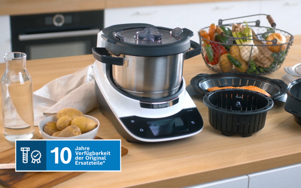 Küchengeräte, Kochutensilien und frische Produkte auf einem Holztisch. Kochgerät Cookit aus Edelstahl mit Bedienfeld