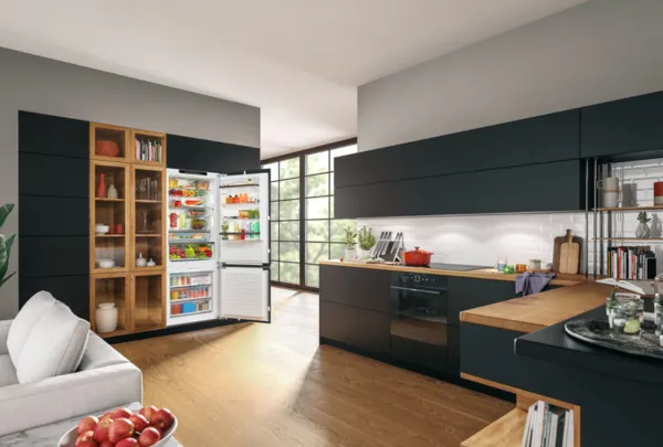 מקרר של בוש עם דלת פתוחה בתוך מטבח מודרני עם ארונות מטבח שחורים בעלי שיש עץ