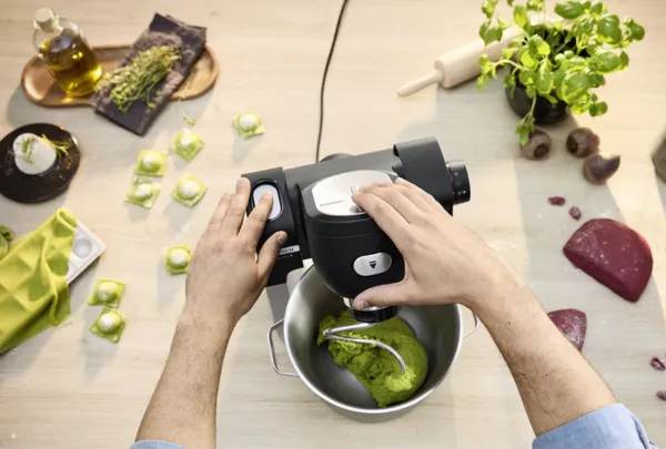 אדם אוחז ומתפעל מיקסר של בוש בצבע שחור כשלצדו שמן, צמחים ומוצרי מזון