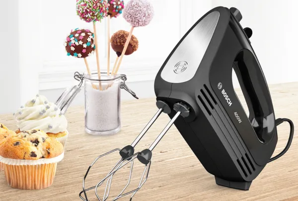 מיקסר של בוש בצבע שחור מונח על שולחן לצד מאפינס ומקלות עם כדורי שוקולד