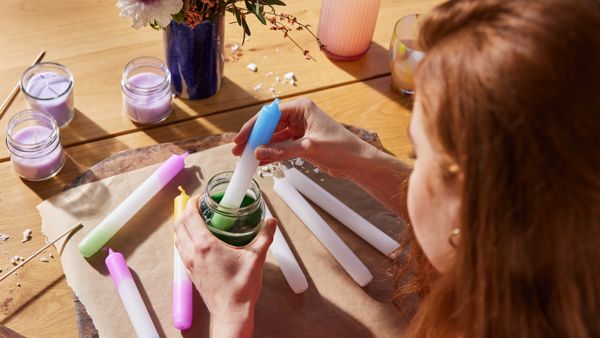 Es ist eine junge Frau zu sehen, die Kerzen in grünes Wachs taucht, um sie einzufärben.