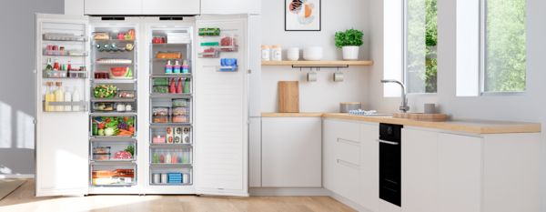 Модерна кухня с хладилник с две врати, пълен с пресни продукти и напитки, и разположена наблизо трапезна маса.