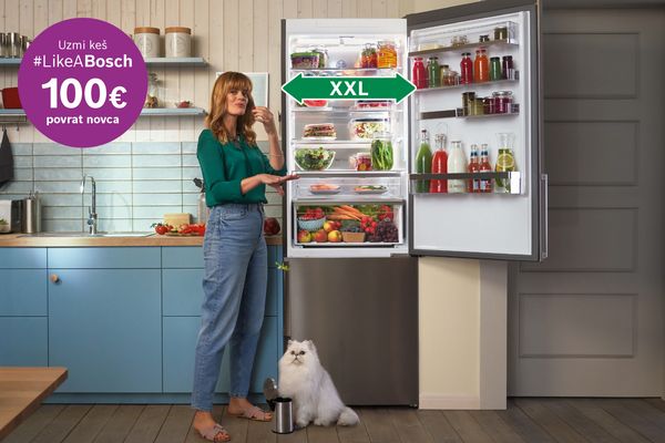 Moderna kuhinja s velikim otvorenim hladnjakom punim hrane i pića, bijela mačka sjedi na podu. 