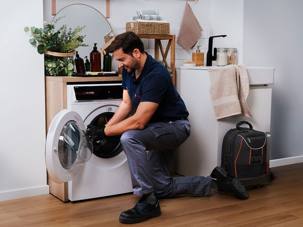 Bilden visar en servicetekniker fr&aring;n Bosch som reparerar en tv&auml;ttmaskin i ett hem.