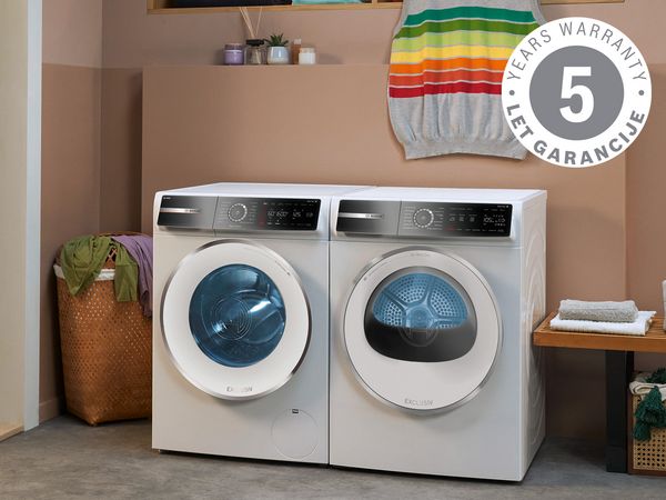 Pralni in su&scaron;ilni stroj BSH v sodobni pralnici, z oblačili vidnimi v oknih, obdan s ko&scaron;i in leseno klopjo. 