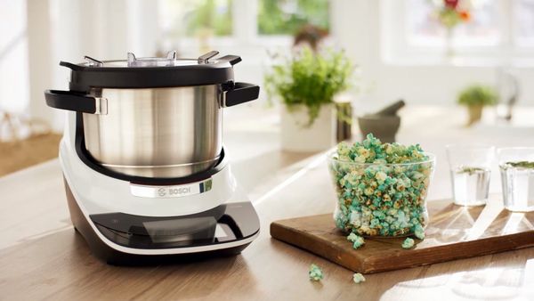 Bosch Cookit mit XL-Topf neben einer Sch&uuml;ssel mit buntem Popcorn auf der K&uuml;chenarbeitsfl&auml;che.