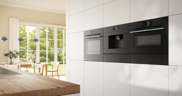 Nowoczesna kuchnia z drewnianym blatem, czarny sprzęt, p&oacute;łki i duże okno.