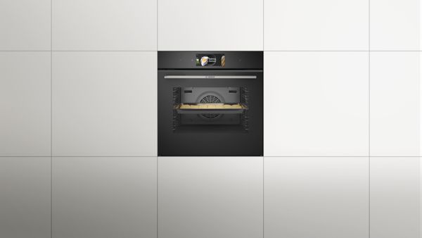 Фурна за вграждане с дигитален дисплей, рафтове със съдове и дървени шкафове на заден план.