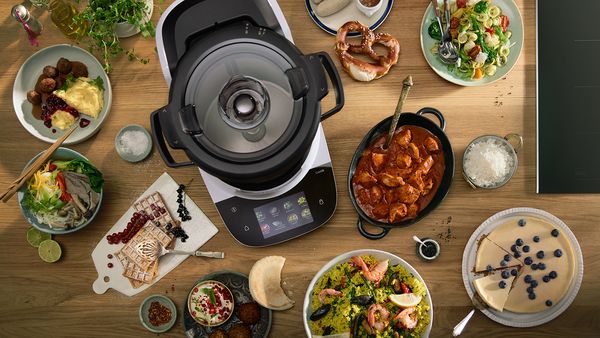 Bosch Cookit in der Draufsicht, umgeben von verschiedenen zubereiteten Gerichten auf einem Tisch.