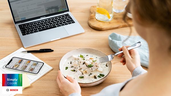 Person nutzt Smartphone zur Rezeptbewertung beim Essen eines zubereiteten Gerichts.
