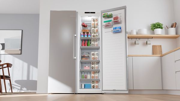 Отворен, модерен фризер с единична врата в стилна кухня, показващ различни замразени храни и организирани отделения.