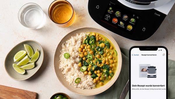 Fertiges Gericht neben Smartphone mit Home Connect App, die ein Rezept f&uuml;r den Bosch Cookit konvertiert.