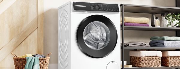 Lavatrice Bosch a carica frontale in una lavanderia domestica, accanto a scaffali con asciugamani e cesti in vimini