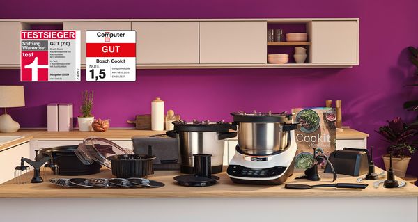 Bosch Cookit K&uuml;chenmaschine mit Kochfunktion und umfangreichem Zubeh&ouml;r auf der Arbeitsfl&auml;che, inklusive Testsieger-Auszeichnungen von Stiftung Warentest und Computer Bild.