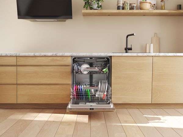 Lavastoviglie da incasso aperta con stoviglie sistemate nei cestelli, integrata in una cucina con mobili in legno