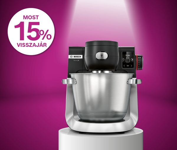 P&oacute;diumon &aacute;ll&oacute;, fel&uuml;lről megvil&aacute;g&iacute;tott Bosch MUM fekete &eacute;s ez&uuml;st konyhai robotg&eacute;p magenta sz&iacute;nű h&aacute;tt&eacute;ren 15%-os piktogrammal mellette.