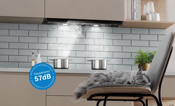 Chat endormi devant la plaque avec des casseroles fumantes et la Hotte Int&eacute;gr&eacute;e Design au-dessus. Graphique indiquant 57 dB de bruit sur l&rsquo;image.