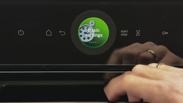 A close-up of a touchscreen displaying an "Basic settings" option being pressed, with start/stop buttons visible.