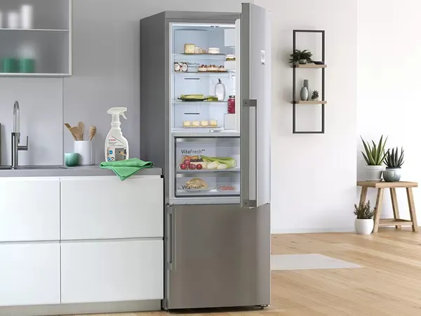 Open stainless refrigerator with Bosch Fridge Cleaner and green cloth on the counter.