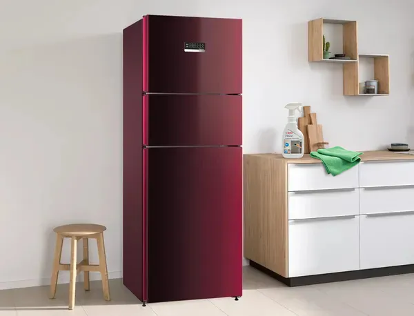 Deep-red, three-door fridge next to a countertop with a Bosch Fridge Cleaner spray bottle and green cloth.