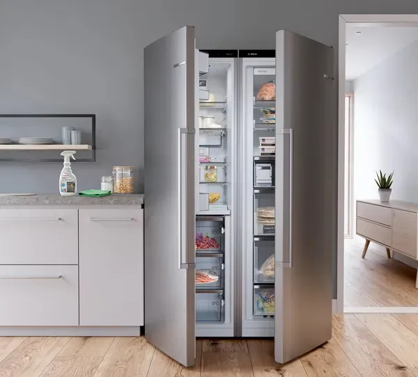 Deep-red, three-door fridge next to a countertop with a Bosch Fridge Cleaner spray bottle and green cloth.