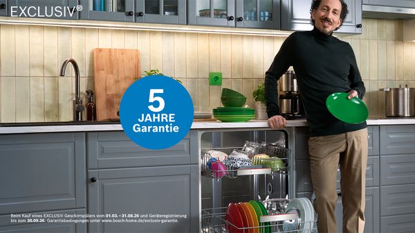 Person in moderner K&uuml;che l&auml;dt Geschirr in Geschirrsp&uuml;ler mit '5 Jahre Garantie'.