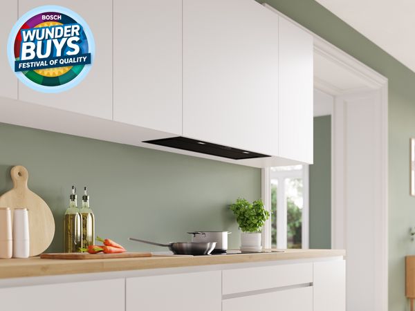 Bosch under-cabinet rangehood in a modern white kitchen with green backsplash and timber benchtop. 