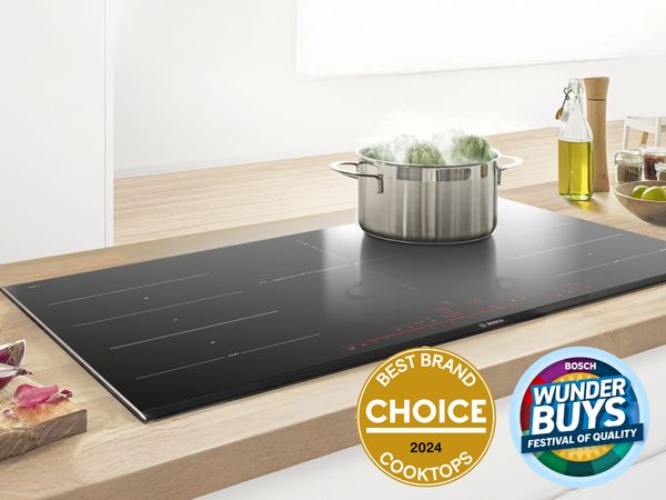 Bosch flush-mounted black induction cooktop on a timber benchtop with steaming pot and Choice Best Brand badge. 