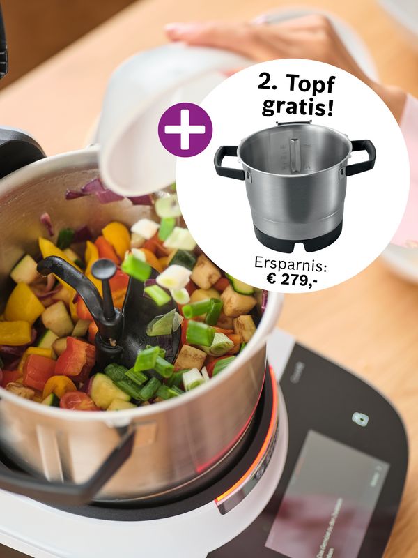 Eine Person f&uuml;llt Gem&uuml;se in eine Cookit K&uuml;chenmaschine. Daneben wird ein zweiter Topf als Gratis-Zugabe beworben, mit einem Ersparnis von 279 Euro.