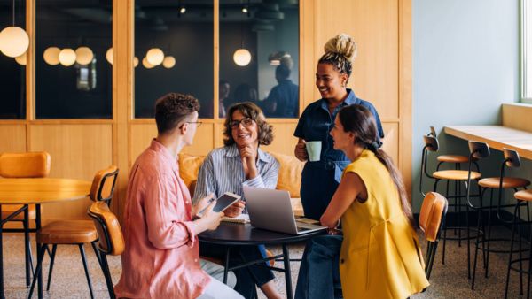 Vier Personen diskutieren entspannt bei Kaffee um einen Laptop, informelles Teammeeting im modernen Caf&eacute;.