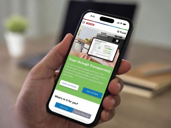Hand h&auml;lt Smartphone mit Bosch Q‑Trust‑Seite: Vertrauen durch Transparenz, Zertifikat pr&uuml;fen.