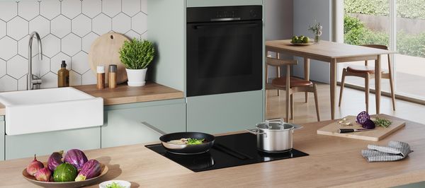 Bilden visar ett modernt gr&ouml;nt k&ouml;k med induktionsh&auml;ll med inbyggd fl&auml;sk och en ugn fr&aring;n Bosch.
